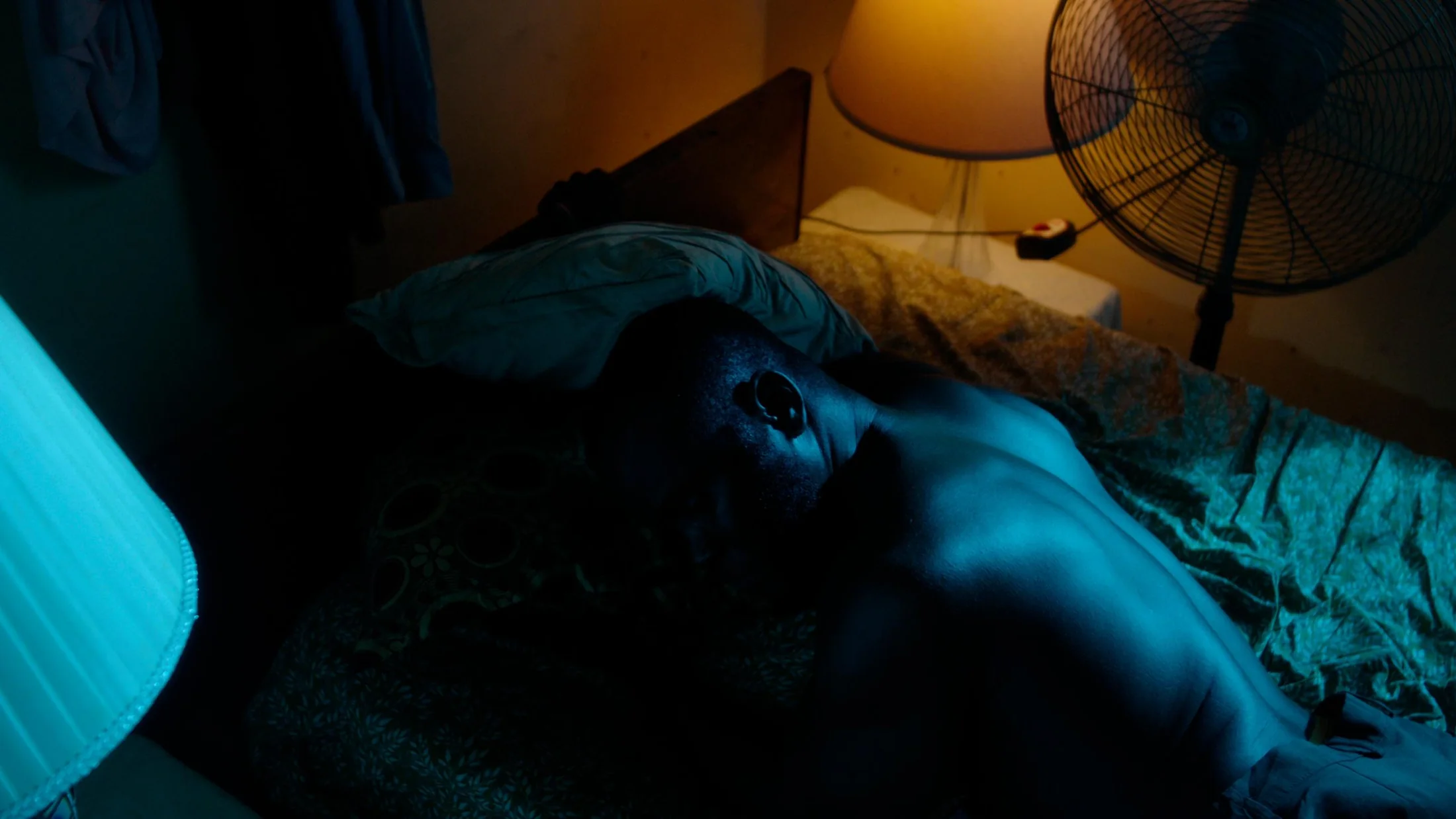 A person resting on a bed in a dim blue-and-amber room