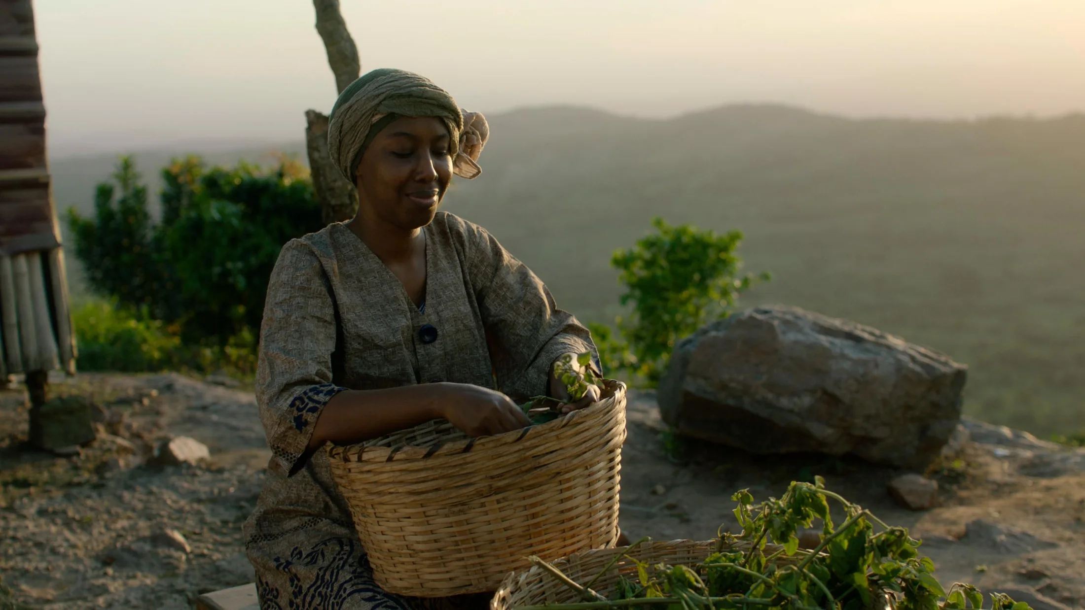 A woman holding a woven basket on a sunlit hillside