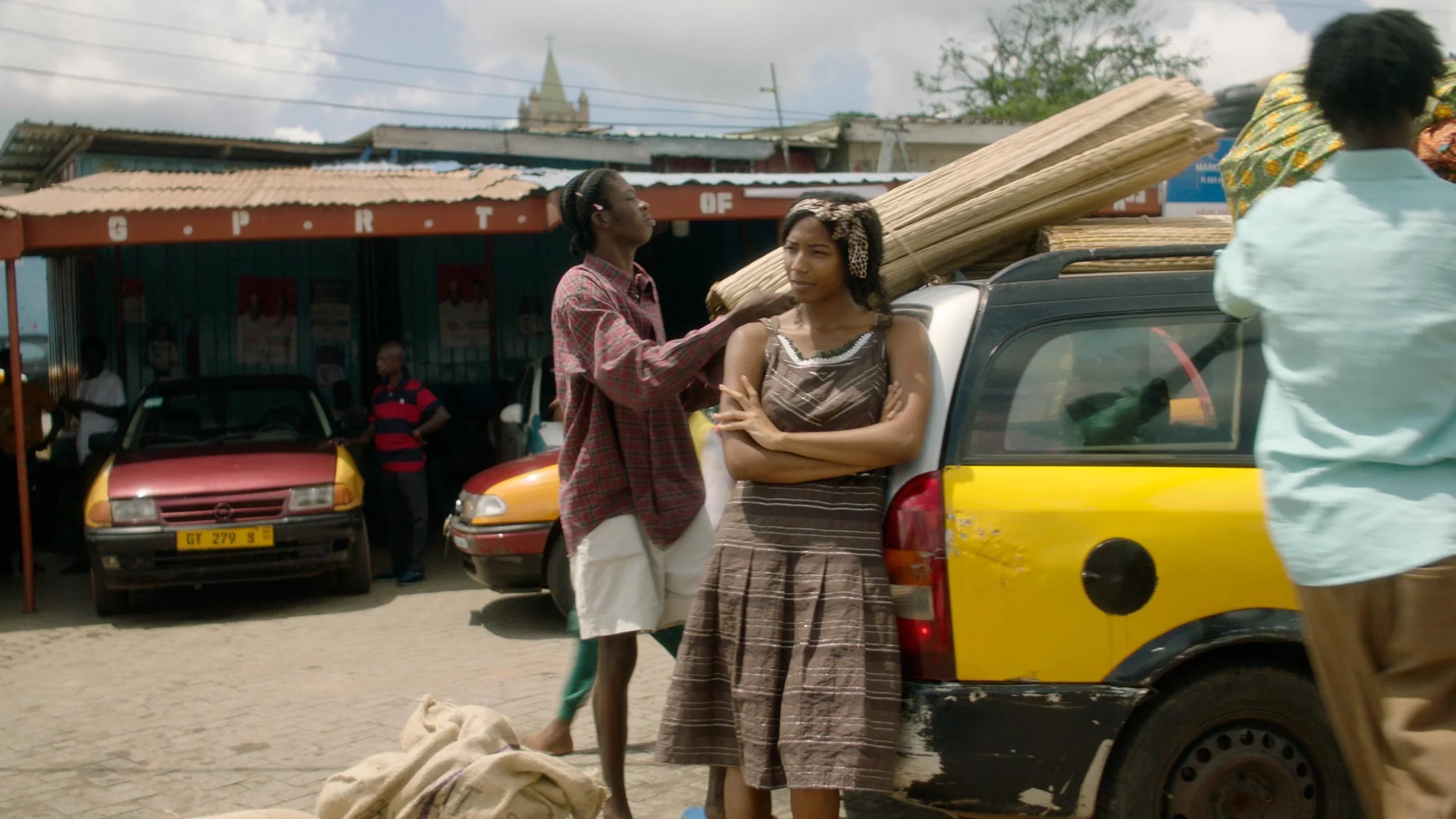 Three women talking beside a yellow taxi in an urban courtyard